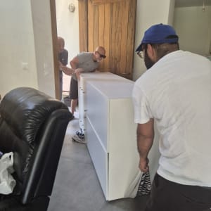 שלושה אנשים מזיזים רהיט גדול דרך דלת פתוחה