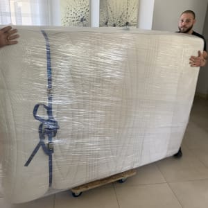 שני אנשים מעבירים מזרן עטוף בניילון על עגלה