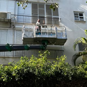 אדם על פיגום מול תריסים בבניין