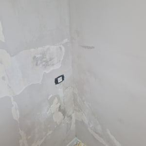 קיר מתקלף עם דלי צבע אדום על הרצפה