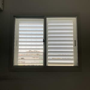 תריסים לבנים על חלון עם אור חיצוני