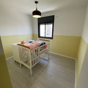 חדר צבוע בצבעים לבן וצהוב עם מיטת תינוק