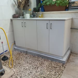 ארון עץ לבן עם ידיות מתכת על משטח חצץ