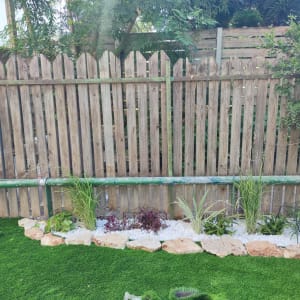 ערוגת גינה עם צמחים ואבנים על דשא סינתטי