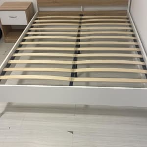 מסגרת מיטה מעץ עם קרשים, ליד שידה קטנה