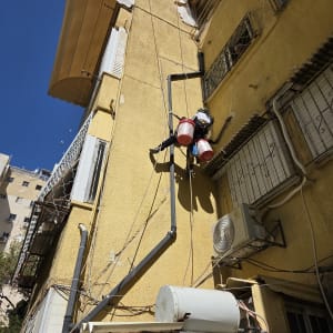 אדם עובד בגובה על קיר בניין עם ציוד בטיחות