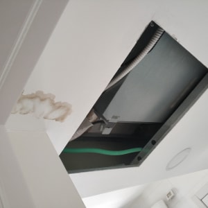 כתם רטיבות על תקרה לבנה ליד פתח תקרה