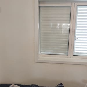 חלון עם תריסים סגורים ומיטה עם כריות