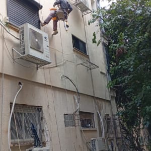 אדם תלוי על חבלים מתקין מזגנים על קיר בניין