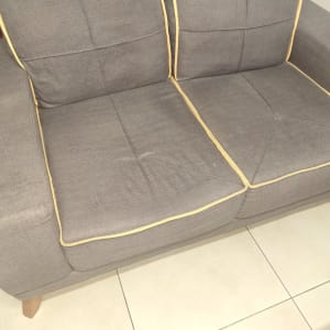 ספה אפורה עם כריות, על רצפת אריחים בהירה.