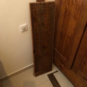 קרש עץ כהה מונח על הרצפה ליד דלת עץ