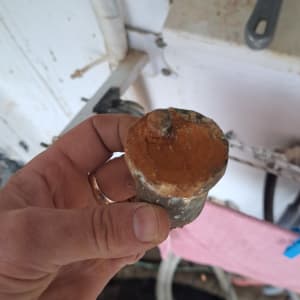חלק מתכת חלוד מוחזק ביד ליד צינורות