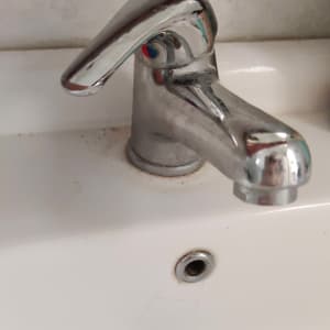 ברז כרום על כיור לבן עם כתמי לכלוך