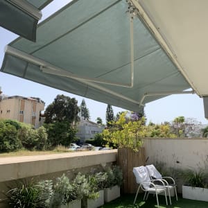 סוככים ירוקים נפתחים מעל מרפסת עם צמחייה