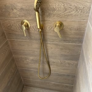 ראש מקלחת מוזהב עם ידיות על קיר עץ