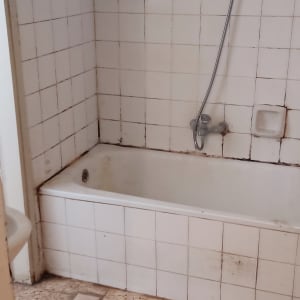 חדר אמבטיה ישן עם אריחים מתקלפים וקירות מוכתמים