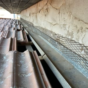 רעפים חומים על גג עם רשת מתכת צמודה לקיר