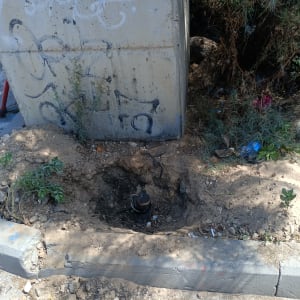 בור באדמה עם צינור חשוף ליד קיר בטון