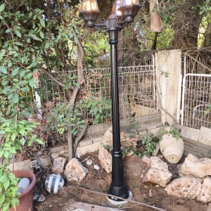 עמוד תאורה עם שלוש מנורות דולקות בגינה