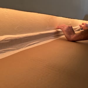 ידיים מניחות סרט דבק על קיר לצורך שיפוץ