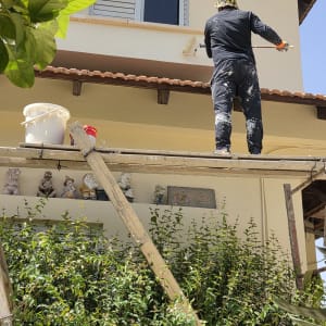 אדם צובע קיר חיצוני בעזרת רולר על פיגום