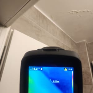 מד חום אינפרא אדום מציג טמפרטורה על קיר עם סימני רטיבות