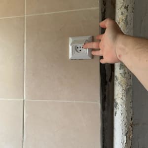 יד נוגעת בשקע חשמלי על קיר אריחים