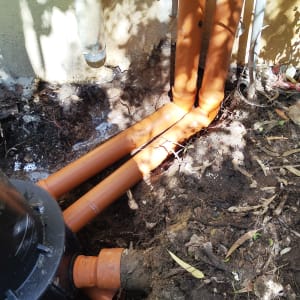 צינורות כתומים מחוברים בקיר חיצוני עם אדמה חשופה