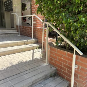 מעקה מתכת על מדרגות ליד קיר לבנים ושיח ירוק