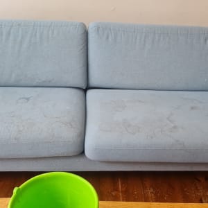 ספה כחולה עם כתמים ודלי ירוק על רצפה מעץ