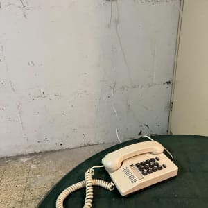 טלפון חוגה ישן על שולחן ירוק עם חוט מחובר לקיר