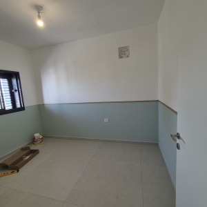 חדר צבוע עם קירות בצבעים שונים, פח צבע וכלי עבודה על הרצפה.