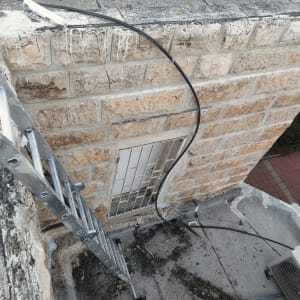 סולם מתכת ליד קיר אבן עם כבל חשמלי