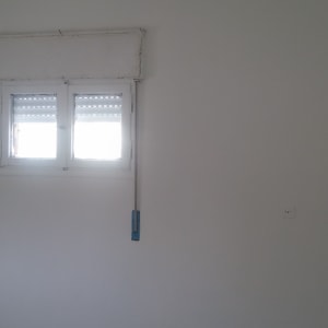 קיר צבוע בלבן עם חלון קטן ומברשת צביעה תלויה