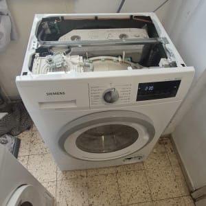 מכונת כביסה פתוחה לתיקון עם ברזים על הקיר