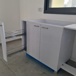 ארון מטבח לבן עם דלת פתוחה ליד חלון