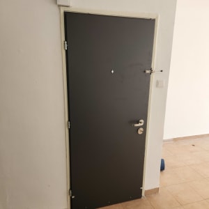 דלת מתכת כהה עם ידית כסופה על רקע קיר לבן