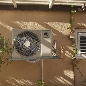 יחידת מיזוג אוויר מותקנת על קיר חיצוני עם צמחייה מסביב