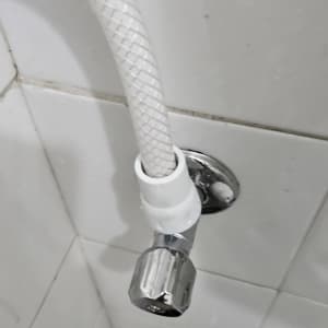ברז ניל זוויתי מחובר לצינור מים גמיש על קיר אריחים לבן