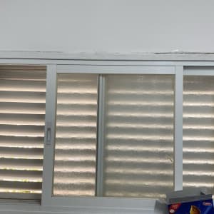 חלון עם תריסים במטבח, מדף עם כוסות וכלים.