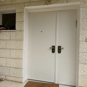 דלת לבנה עם ידיות מתכת ומחצלת חומה