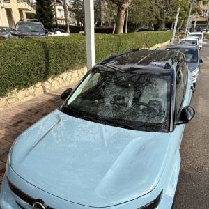 מכונית כחולה חונה ברחוב ליד גדר ירוקה