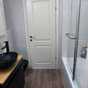 חדר אמבטיה משופץ עם כיור שחור ודלת לבנה