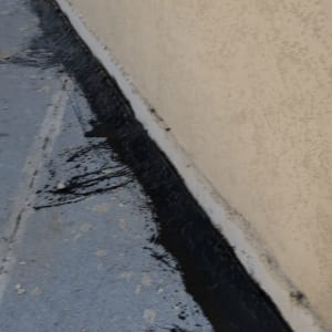 יישום חומר איטום ביטומני שחור בחיבור בין הגג לקיר