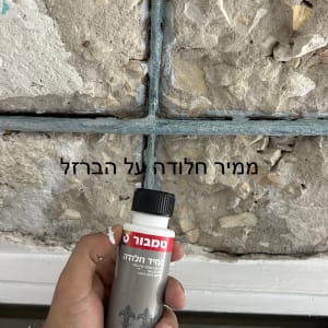 יד מחזיקה בקבוק חומר איטום על קיר בטון