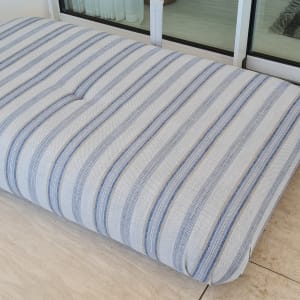 כרית פסים כחולים על רצפת אבן ליד חלון זכוכית.