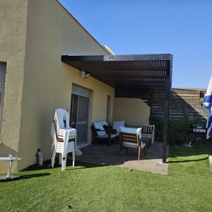 פרגולה מאלומיניום מחוברת לקיר חיצוני של בית