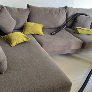 אדם מנקה ספה עם שואב אבק וצינור