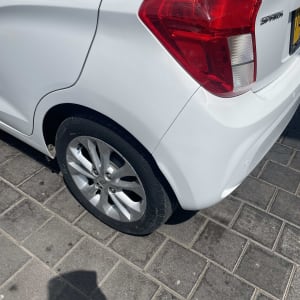 חלק אחורי של רכב לבן עם פנס אחורי וגלגל על מדרכה