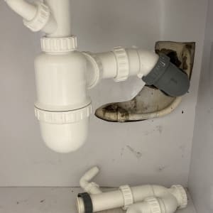 צינורות פלסטיק לבנים מתחת לכיור עם חיבורים אפורים
